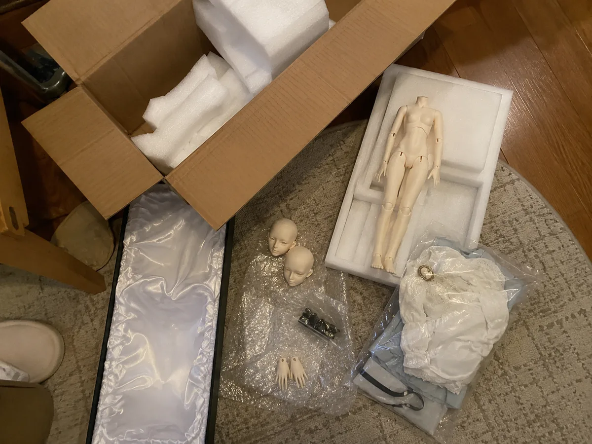 Floor unpacking record: Large box, foam, body parts, clothes, and accessories laid out on a home floor before fit review.